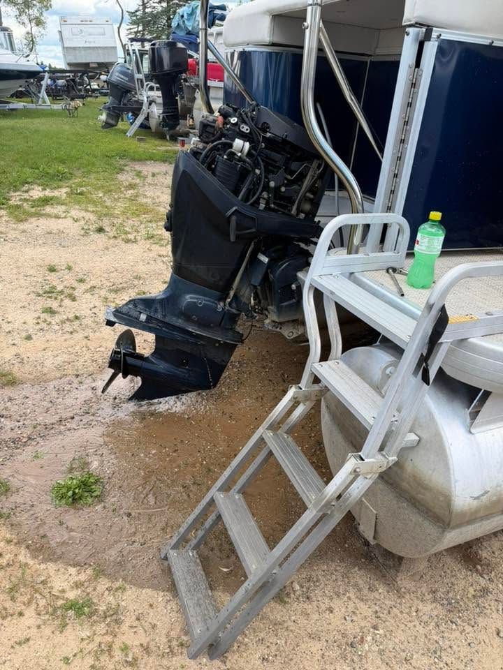 Boat motor leaning beside a white chair and aluminum step ladder on a gravel lot