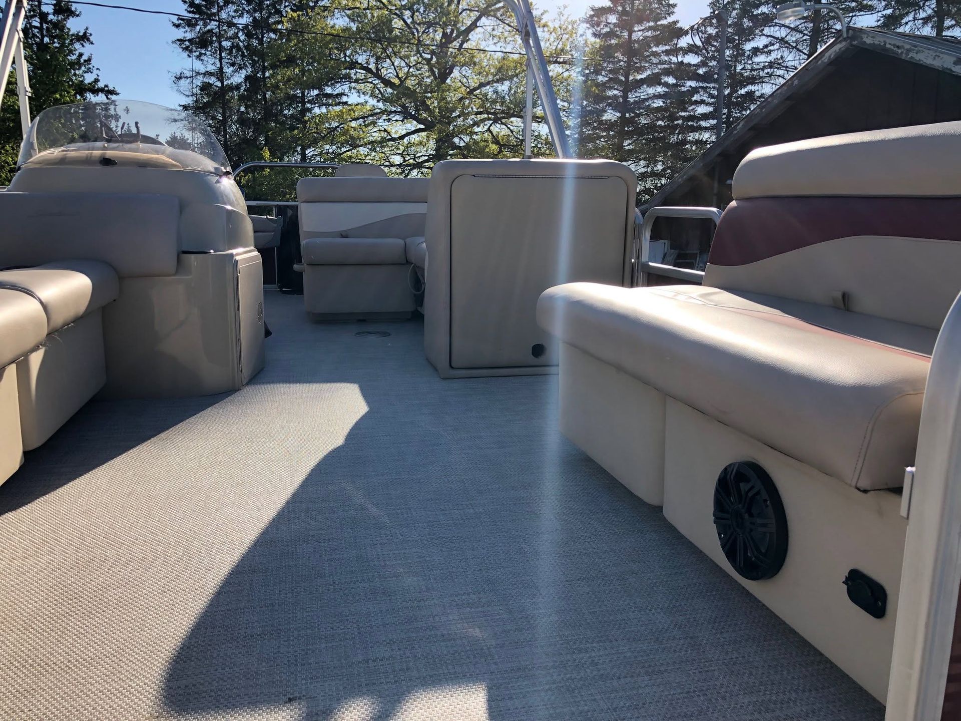 Pontoon boat seating with beige benches and a small table under bright daylight, trees in the background