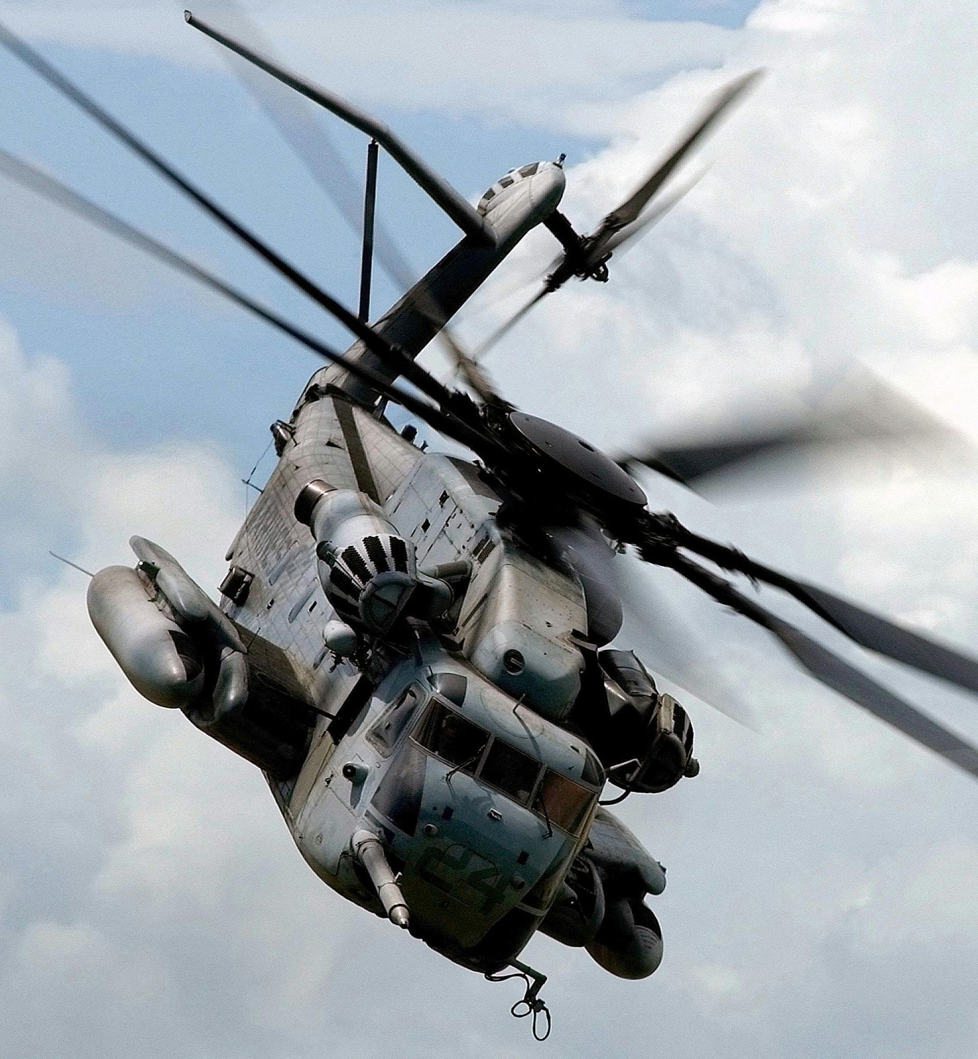 A gray military helicopter banking in mid-air against a cloudy sky.