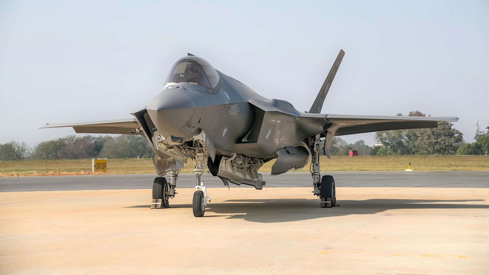 A grey F-35 Lightning II fighter jet sits on a paved runway under a clear blue sky.
