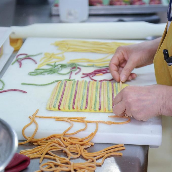 Persona che dispone su un tagliere bianco dei coloratissimi spaghetti di pasta fatti a mano.