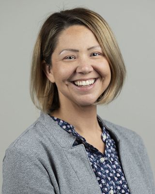A woman wearing a gray jacket and a blue shirt is smiling for the camera.