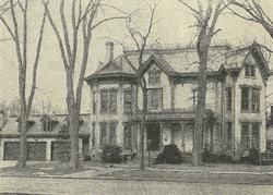 A black and white photo of a large house surrounded by trees.