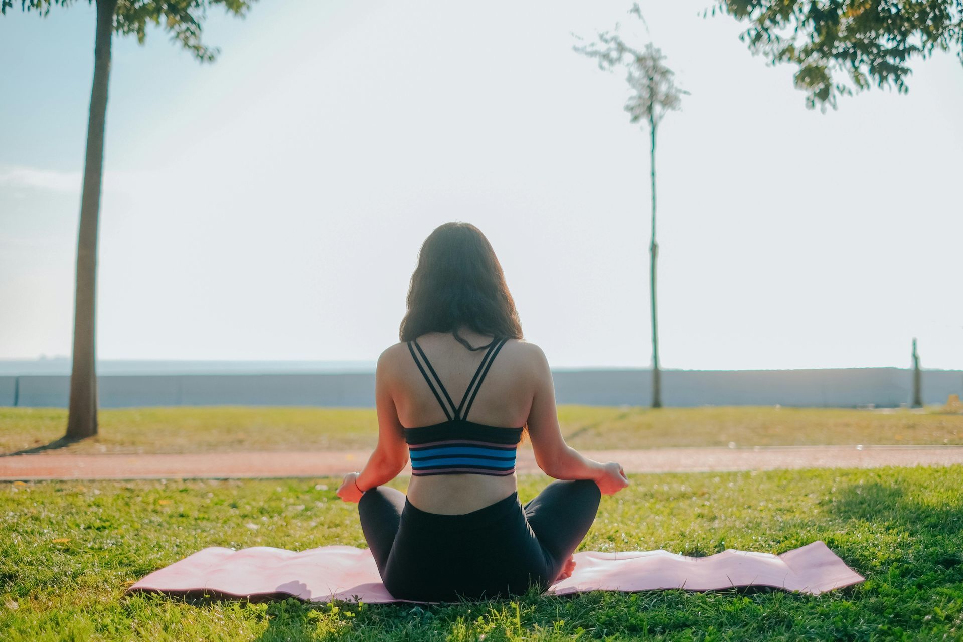 Person sitting in a cross-legged yoga pose on a mat in a park at sunset.