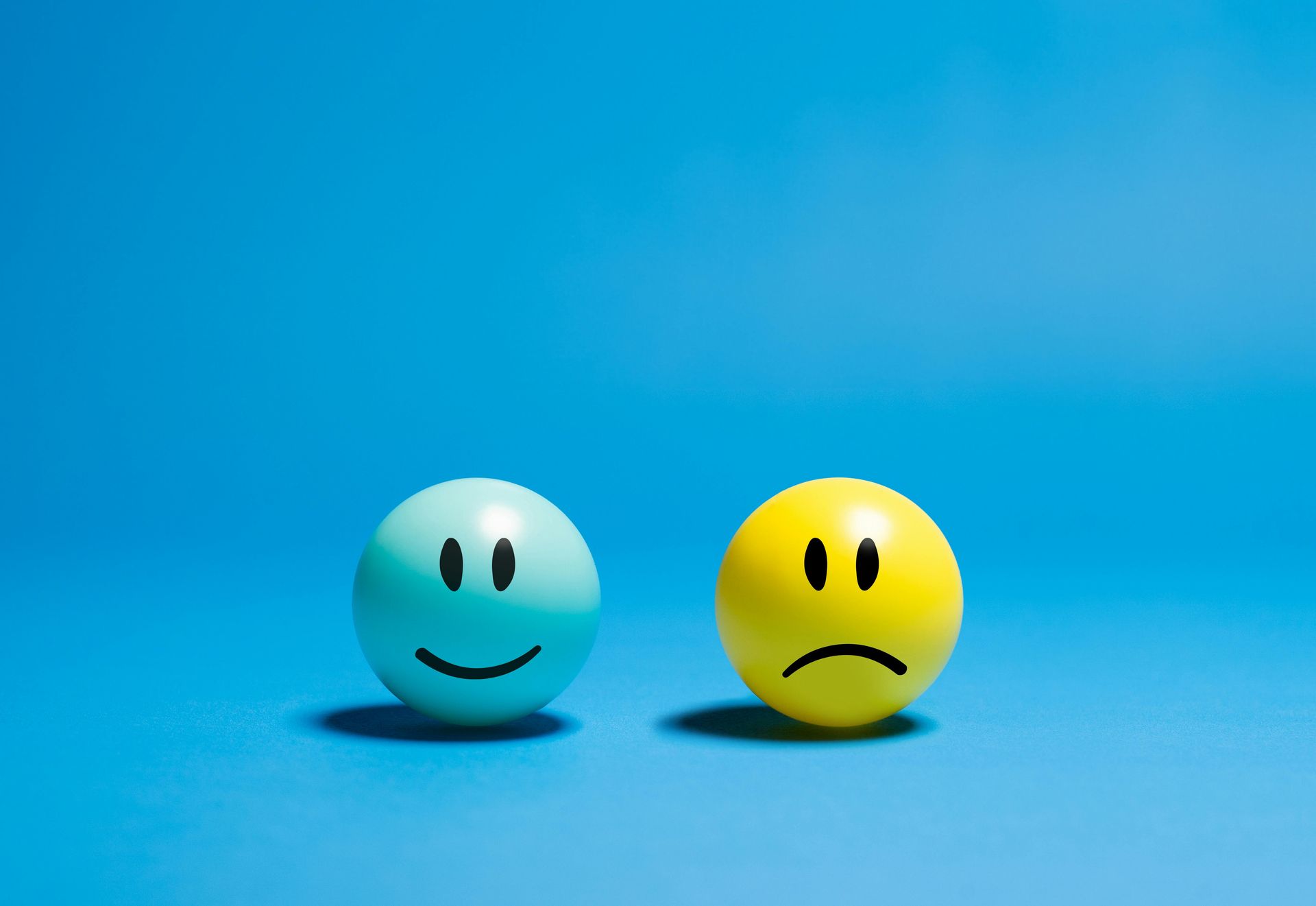 A light blue sphere with a smiling face and a yellow sphere with a sad face sit side by side against a blue background.