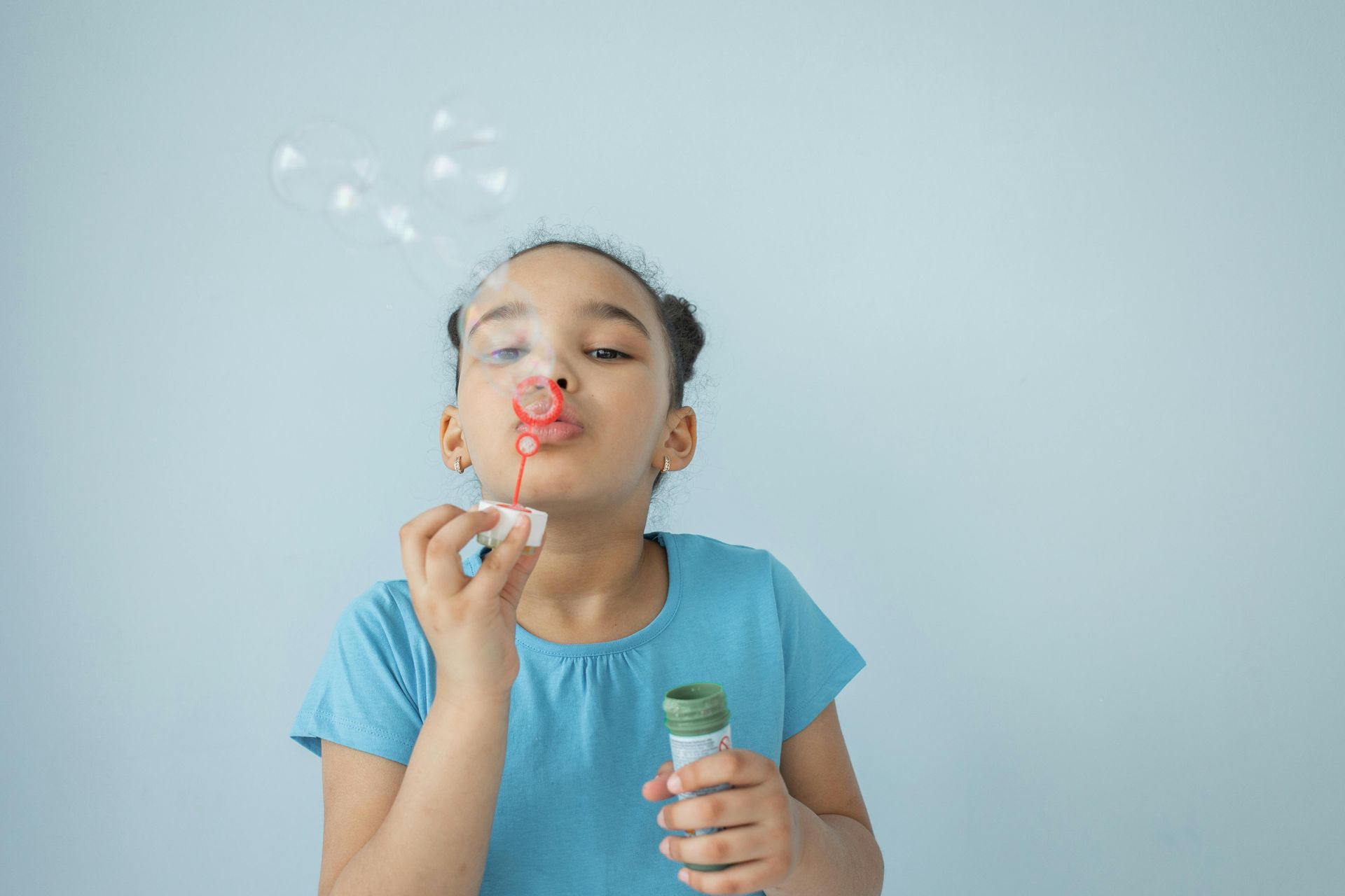 A person in a blue shirt blows bubbles from a small wand against a light blue background.