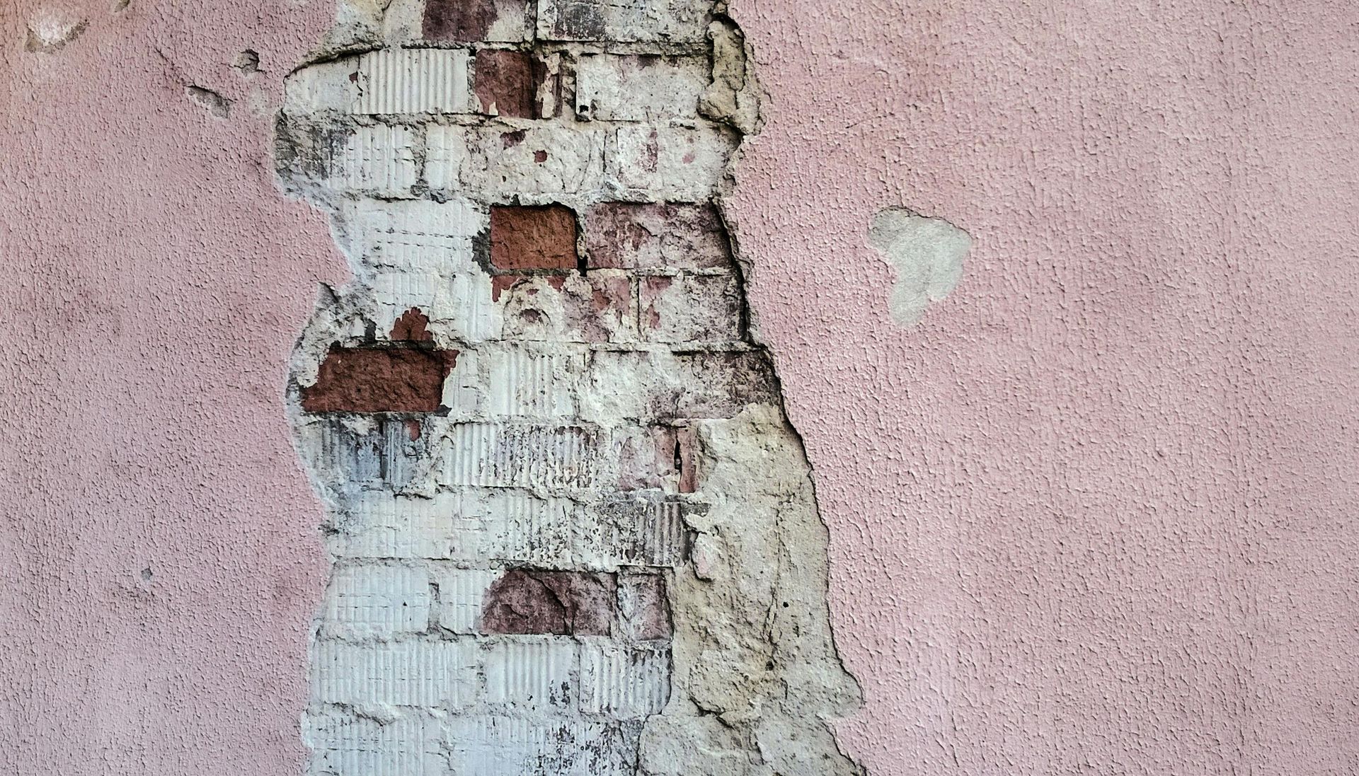 Exposed brick wall section, with pink stucco. Some brick missing, revealing mortar and red brick.
