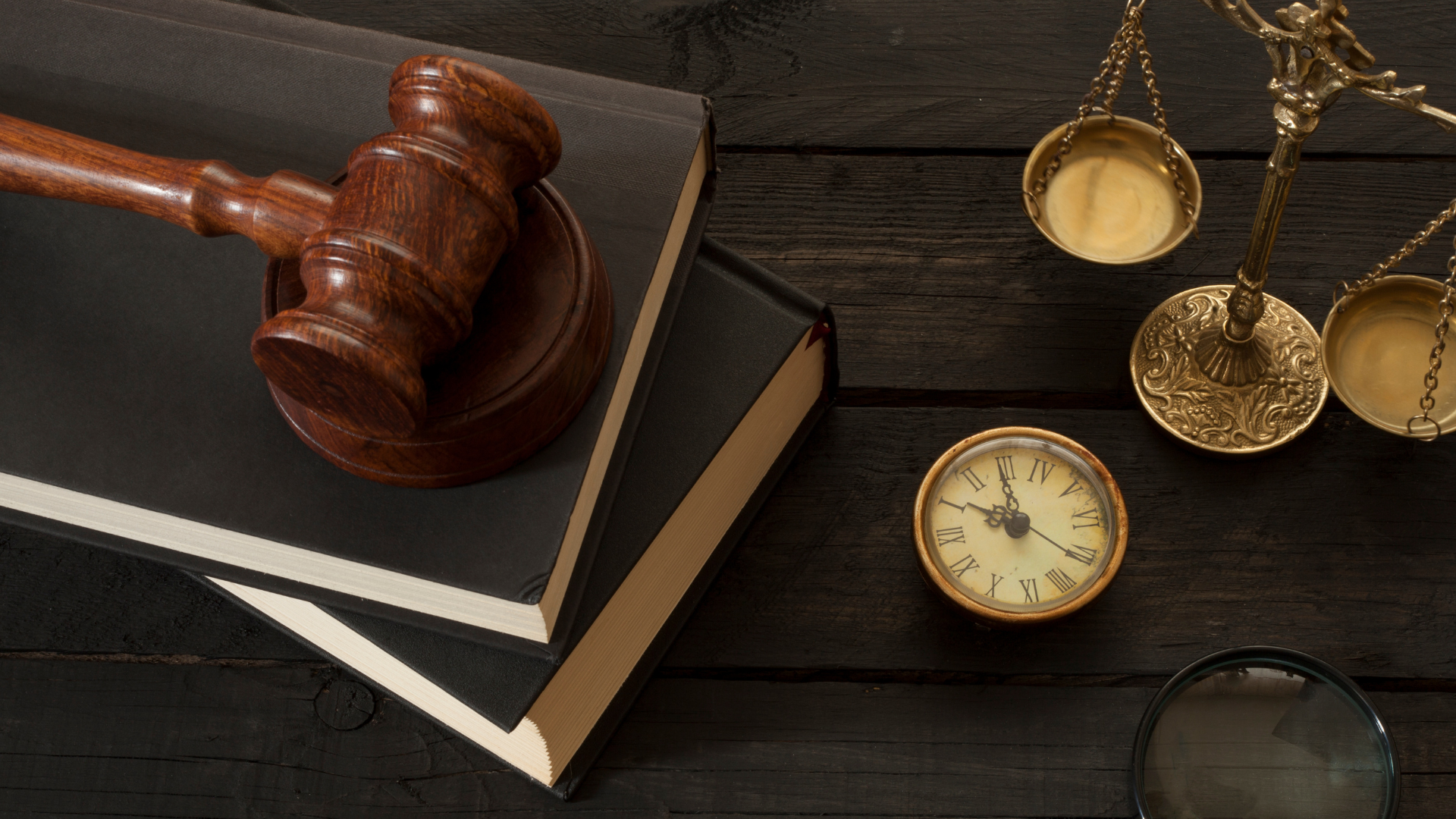 A judge 's gavel , scales of justice , and a clock are on a wooden table.