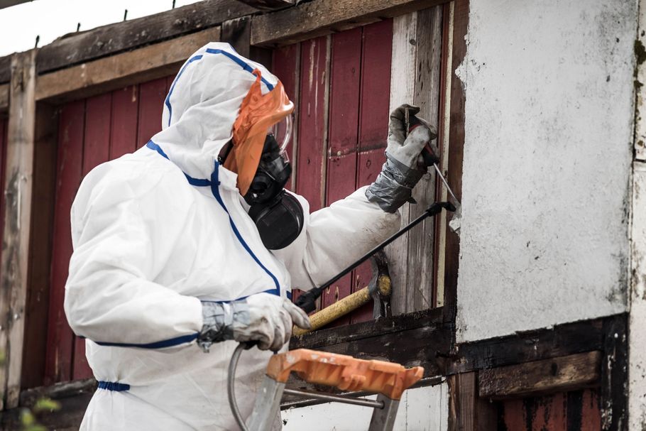 Person in white protective suit spray-painting a damaged wall beside a red door