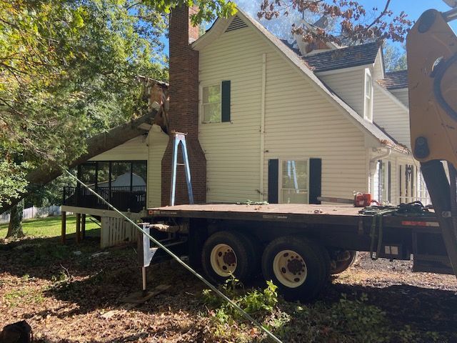 White house with black shutters, a porch, and a chimney; a flatbed trailer is parked nearby.