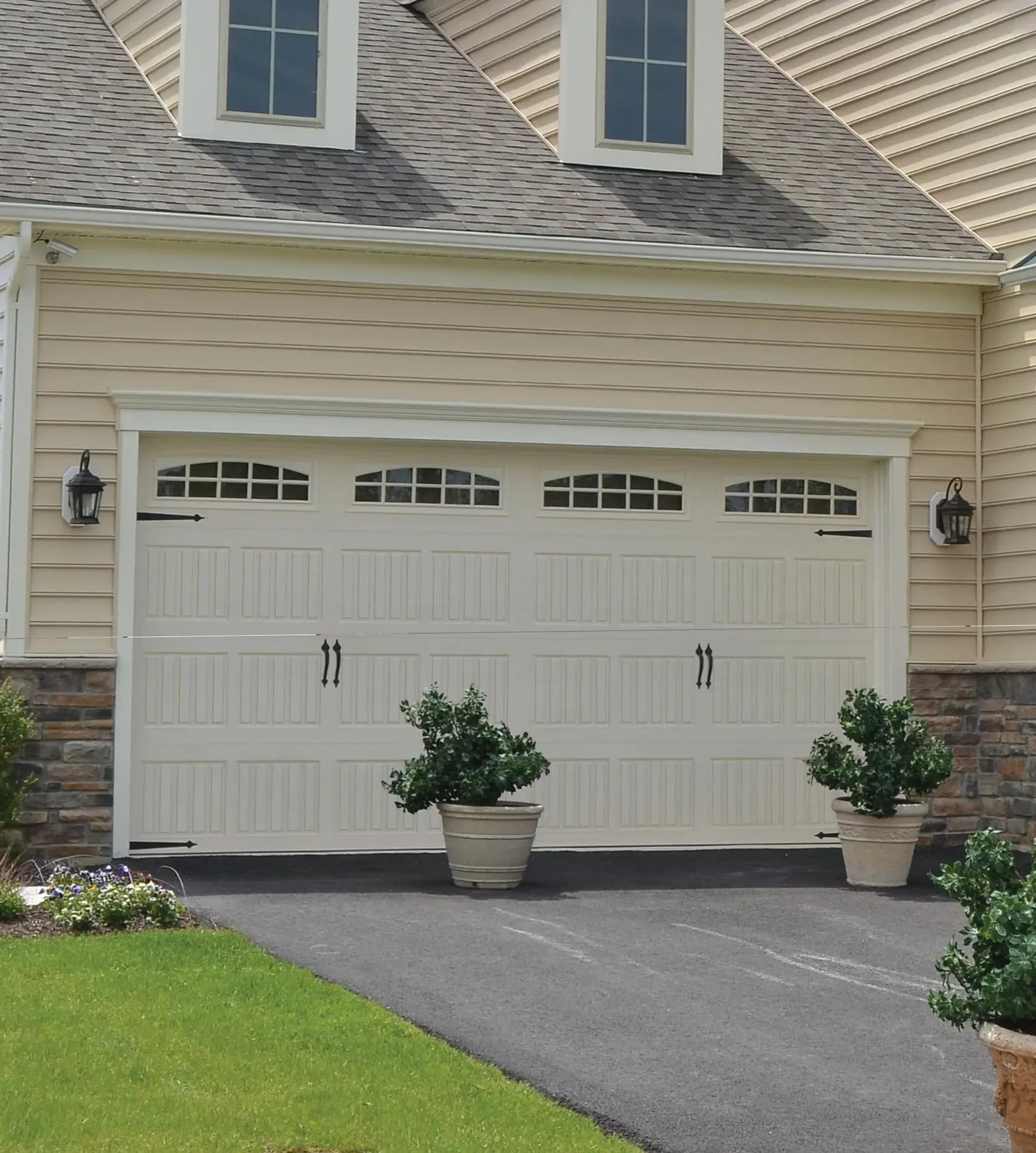 A white garage door with a pergola structure in front of a tan house with a tiled roof.