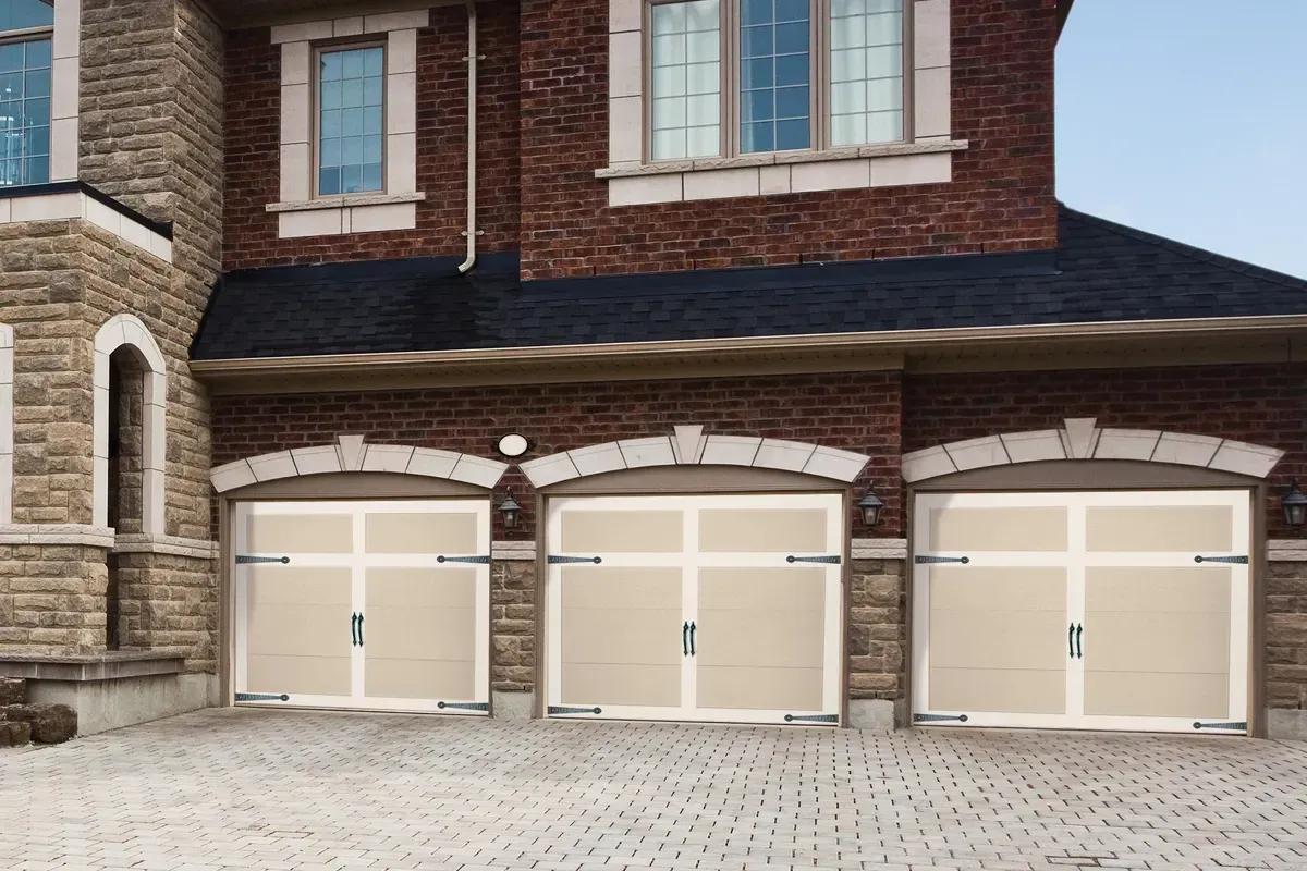 A house exterior featuring three cream-colored carriage-style garage doors with arched brick frames and dark stone siding.