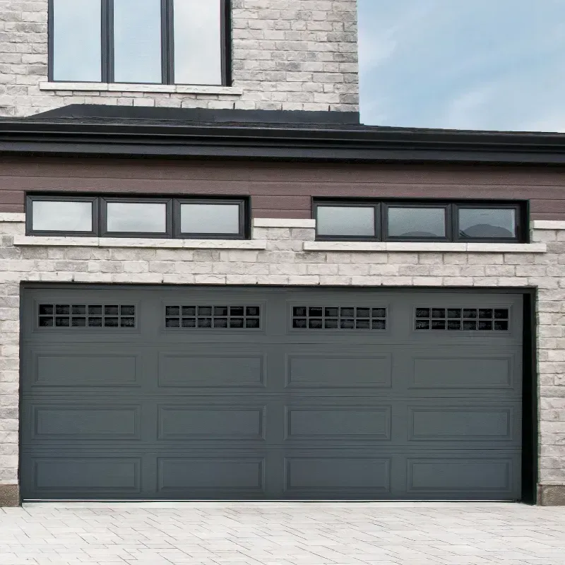 A dark gray garage door with windows, set in a stone facade with rectangular windows above the garage.
