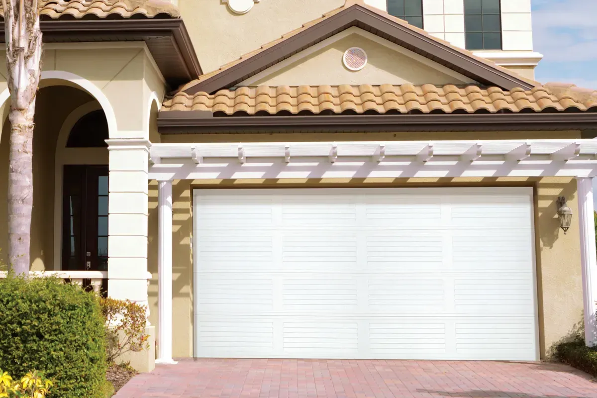 A modern residential home with a white garage door, pergola, and tan exterior, viewed from the driveway.