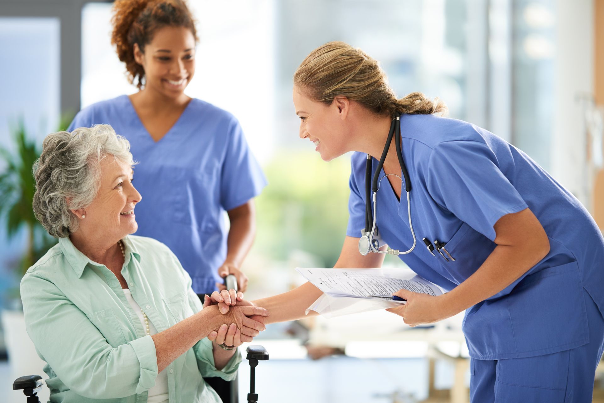 A nurse is shaking hands with an elderly woman in a wheelchair.