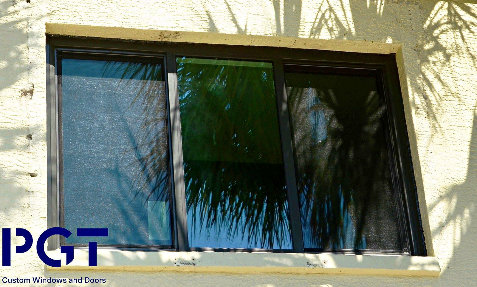 Sunlit window with dark reflective glass and a blue PGT logo in the lower left corner