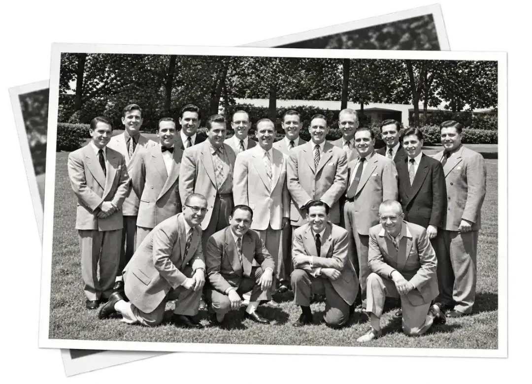 Black-and-white group portrait of men in suits posing outdoors in front of a building
