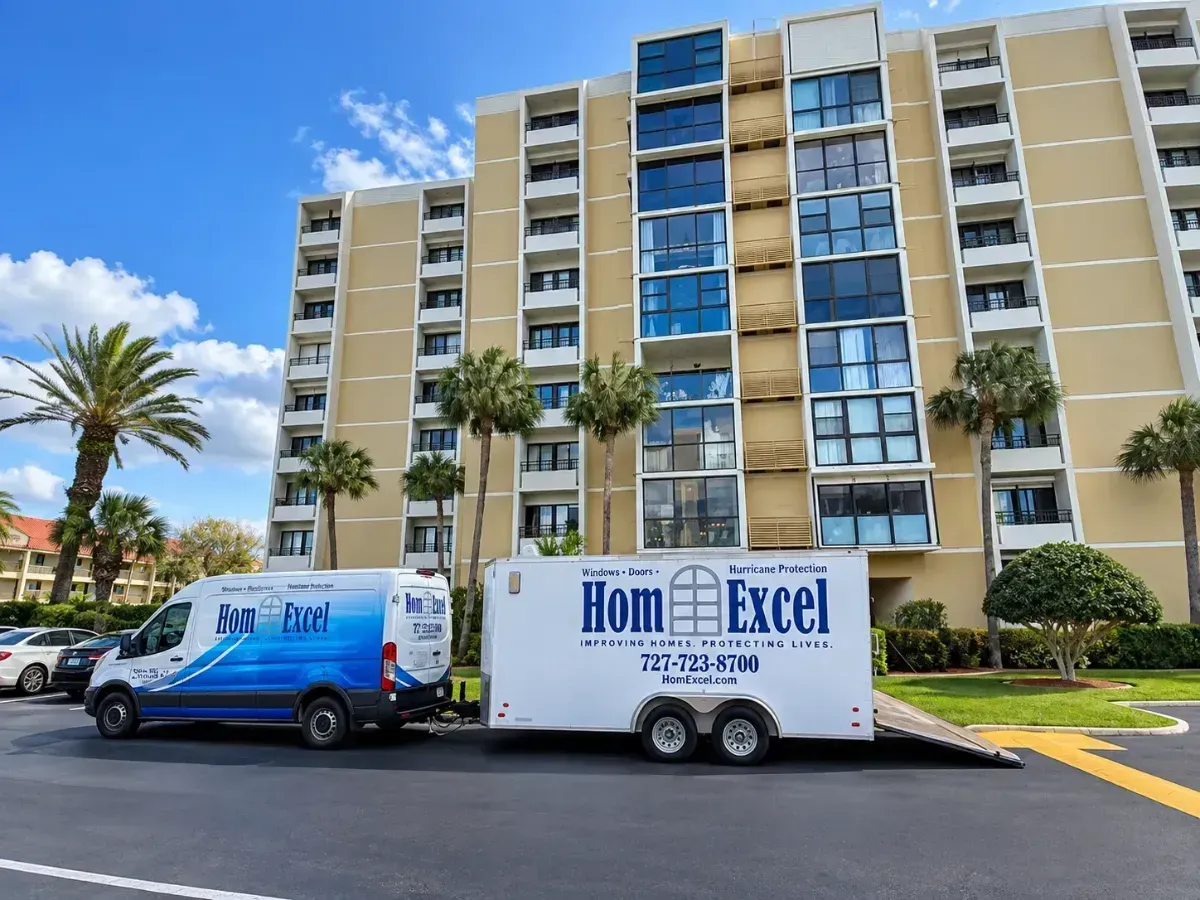 Delivery truck and trailer parked in front of a beige apartment building with palm trees.