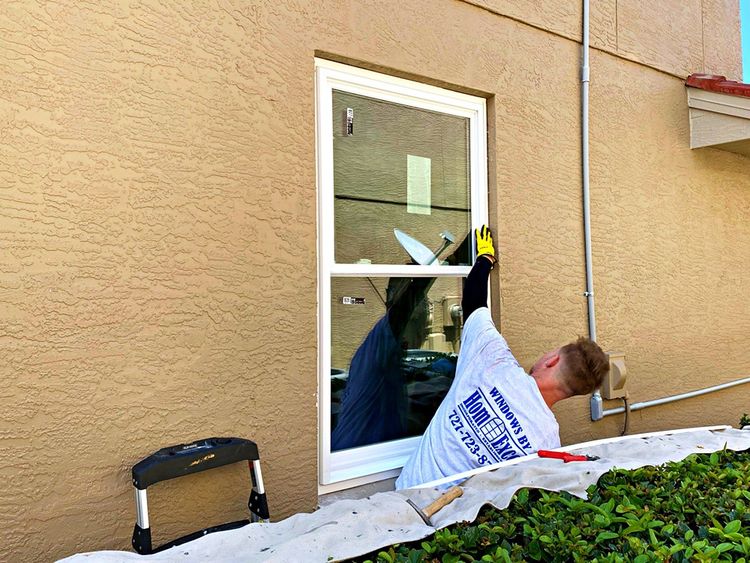 Worker cleaning a glass door on a tan building exterior with a white tarp below.