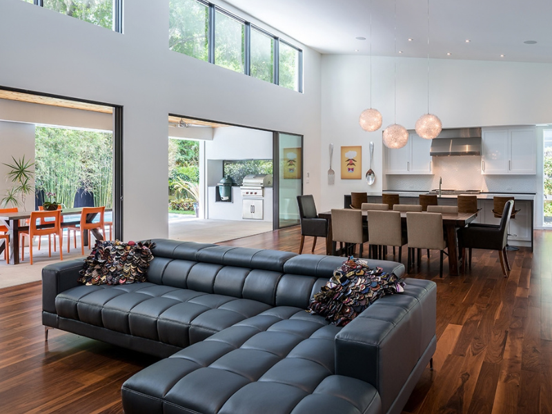 Modern open-concept living room with black sectional sofa, dining area, and kitchen in bright, airy interior