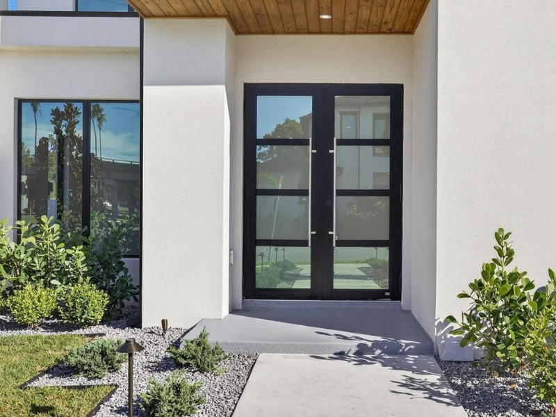 Modern house entry with black double doors, white walls, wood ceiling, and desert landscaping