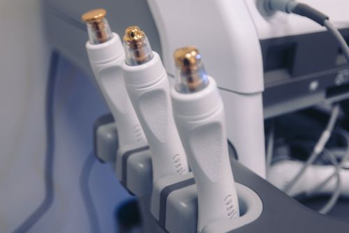 Three white, handheld cosmetic treatment wands with metallic tips stored in a medical device console.