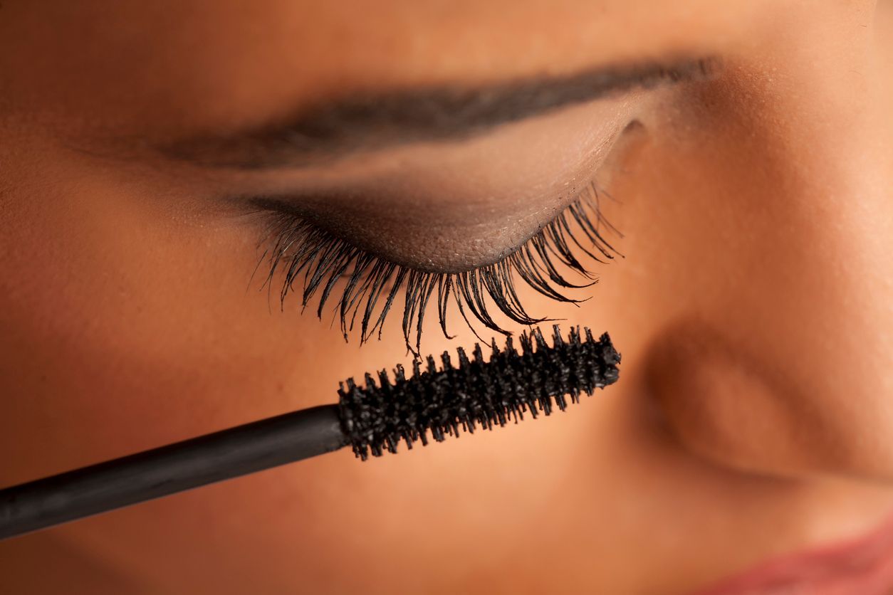 A mascara wand applying black mascara to a person's upper eyelashes.
