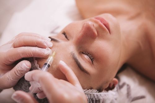 A person receives a cosmetic facial injection in the forehead from a professional wearing gloves.
