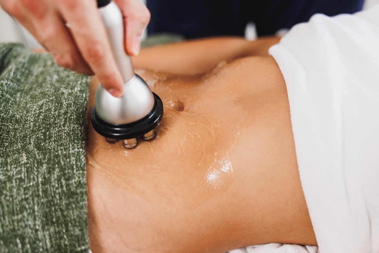 A hand uses a handheld radio frequency device with conducting gel to treat a person's abdomen.