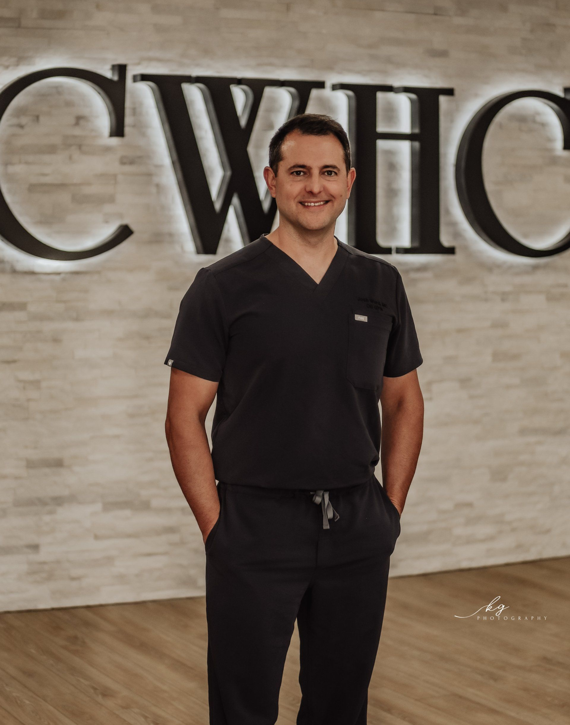 A professional standing in dark scrubs in front of a wall with a large 