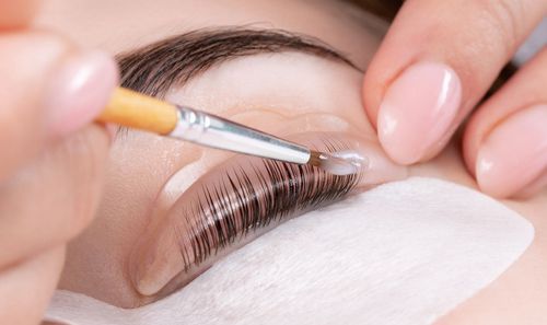 A close-up of a lash lift procedure, where a professional applies a solution to lashes attached to a silicone shield.