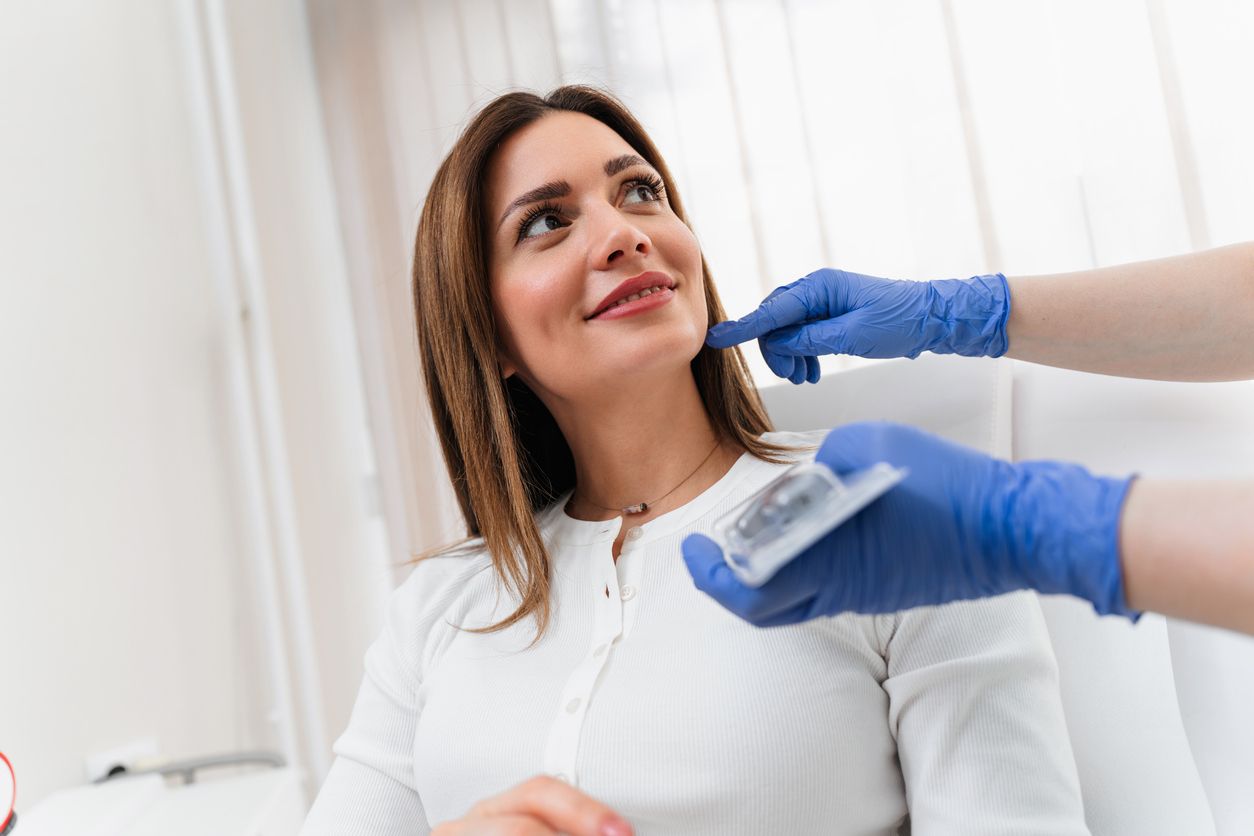 A medical professional in blue gloves examines a patient's jawline during a cosmetic consultation.