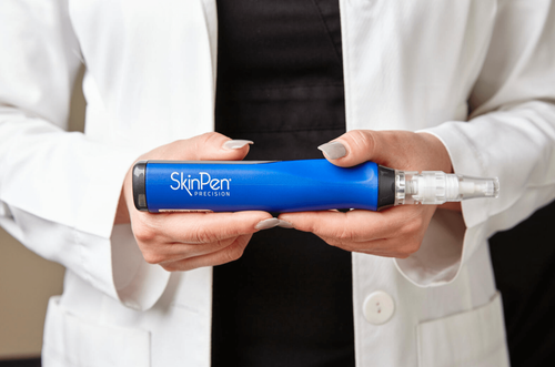 A person in a white lab coat holding a blue SkinPen microneedling device.