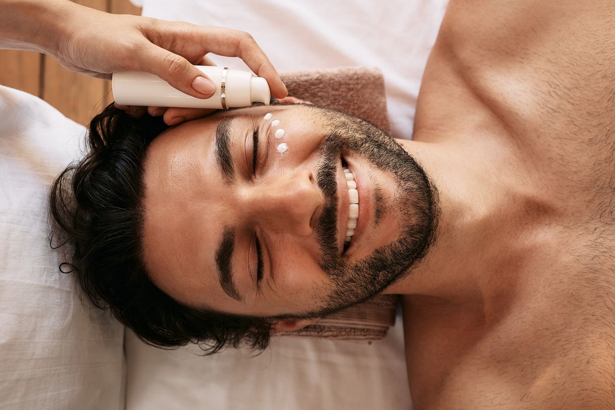 A person lying on a spa bed receives eye cream from a professional applicator.