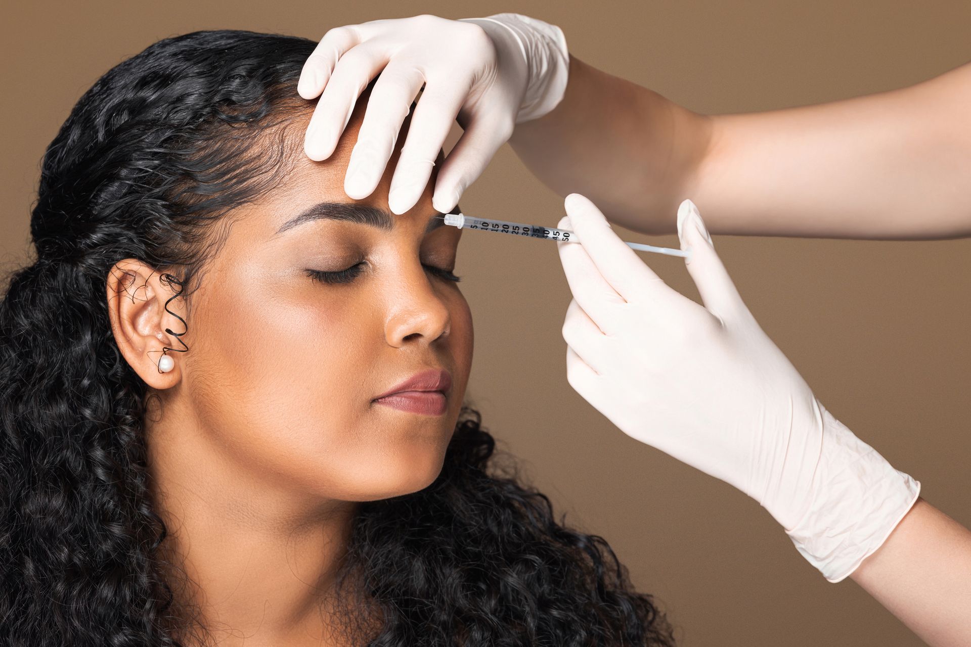 A person receiving a cosmetic injection between the eyebrows from a practitioner wearing white medical gloves.