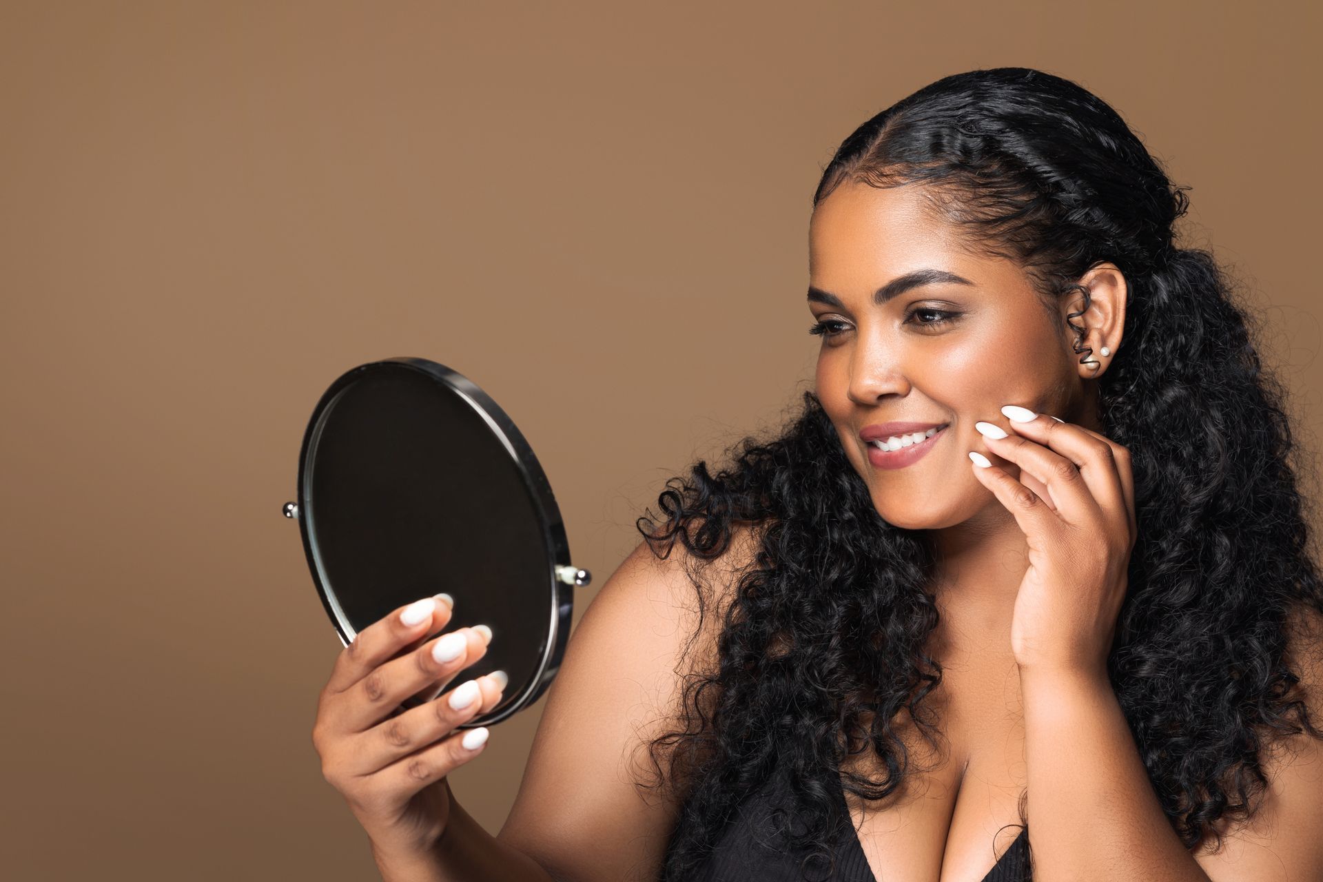 A person smiling while looking at their reflection in a small, round handheld mirror.
