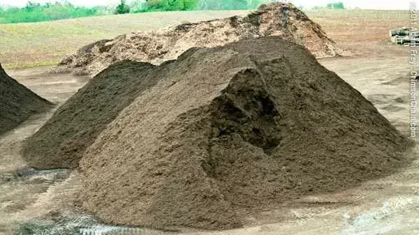 Large pile of dirt or sand at a construction site with fields in the background