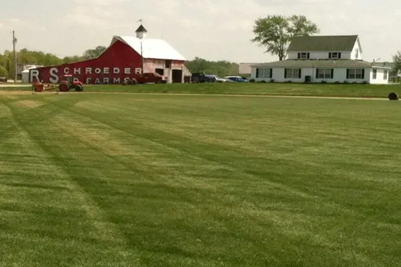 Wide green field with a red barn and white farmhouse under an overcast sky