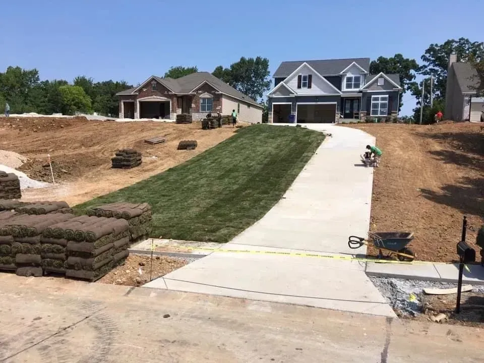 New suburban homes under construction with driveway, lawn, and stacked sod in front yard