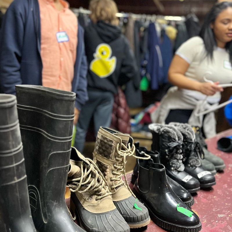 Assorted boots on a market table, with shoppers browsing in the background.