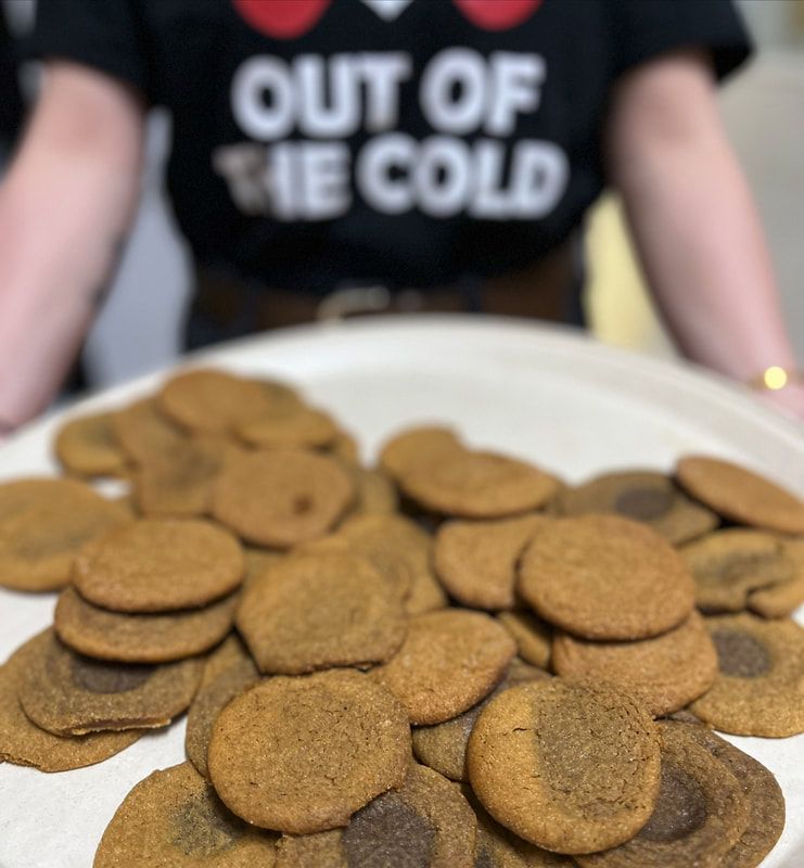 Plate of round cookies with a person wearing a black “OUT OF THE COLD” shirt in the background