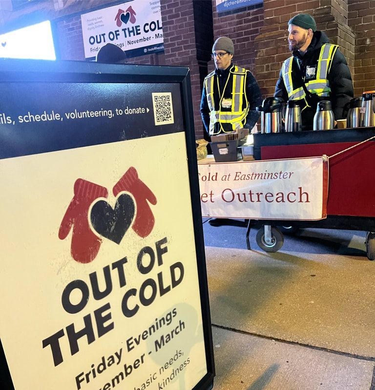 Out of the Cold event sign beside volunteers serving hot drinks at a nighttime outreach table
