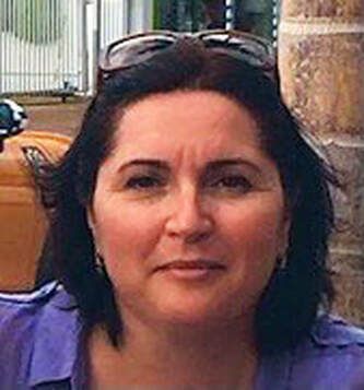 Portrait of a woman with dark hair and glasses on her head, wearing a purple top outdoors