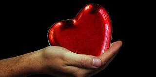 Hand holding a shiny red heart-shaped object on a black background