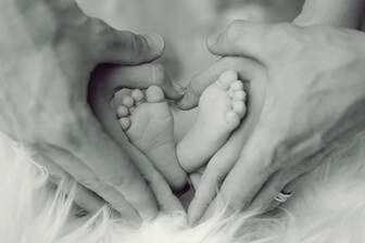 Adult hands cradling two tiny newborn feet against a soft white blanket
