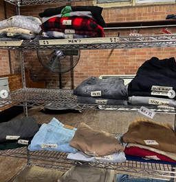 Folded clothing stacked on metal shelves in a store, with sweaters and jeans in various colors.