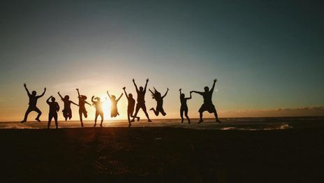 Silhouetted group jumping on a beach at sunset, with glowing sky and water in the background