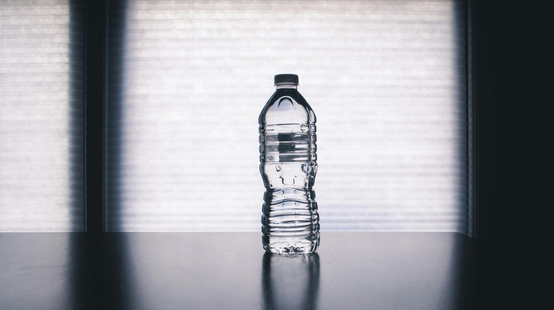 Clear water bottle on a table in front of a bright window.
