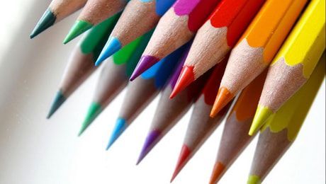 Colored pencils arranged diagonally on a white background, with sharpened tips in multiple bright colors.