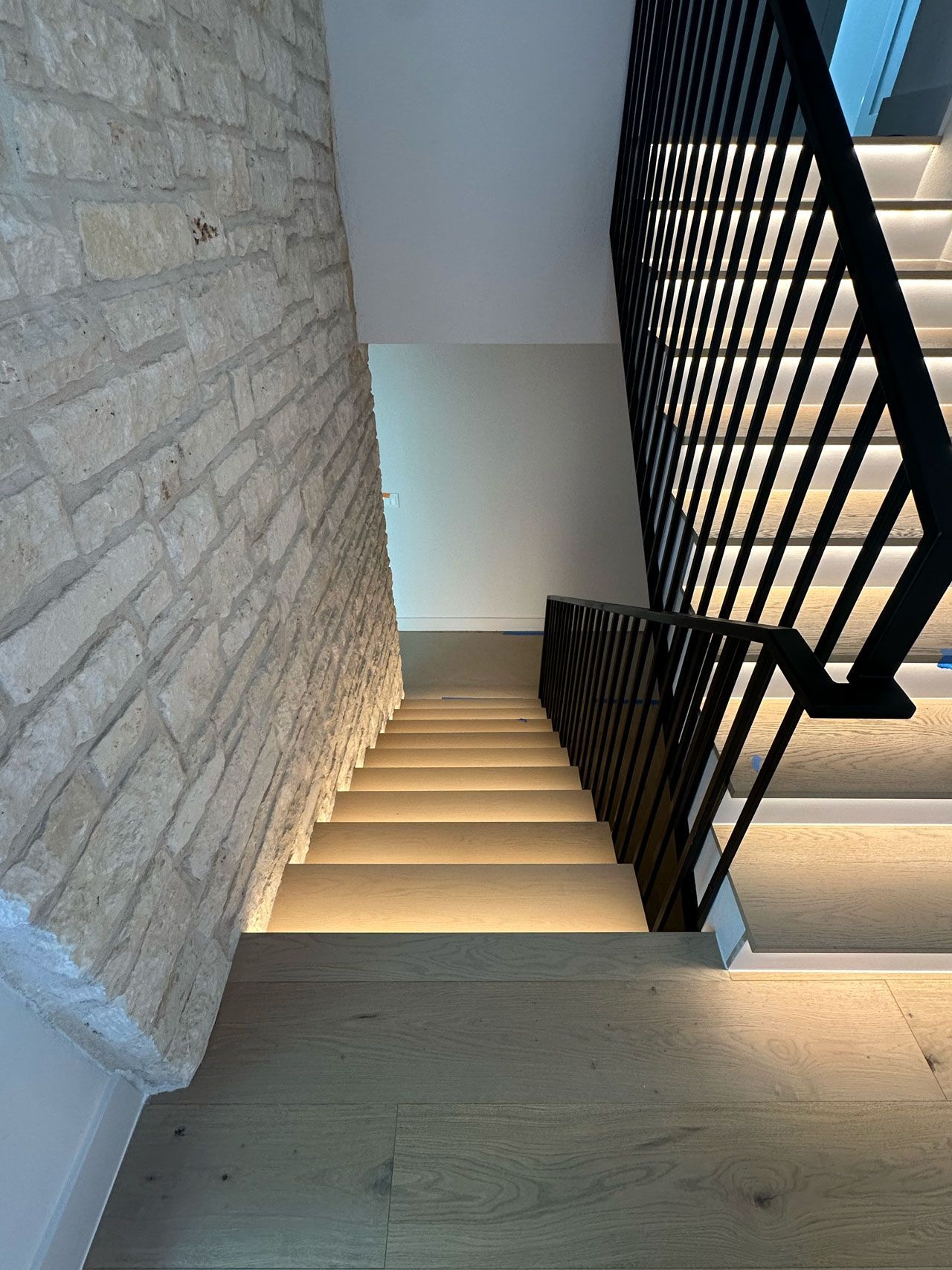 A staircase with a brick wall and a black railing
